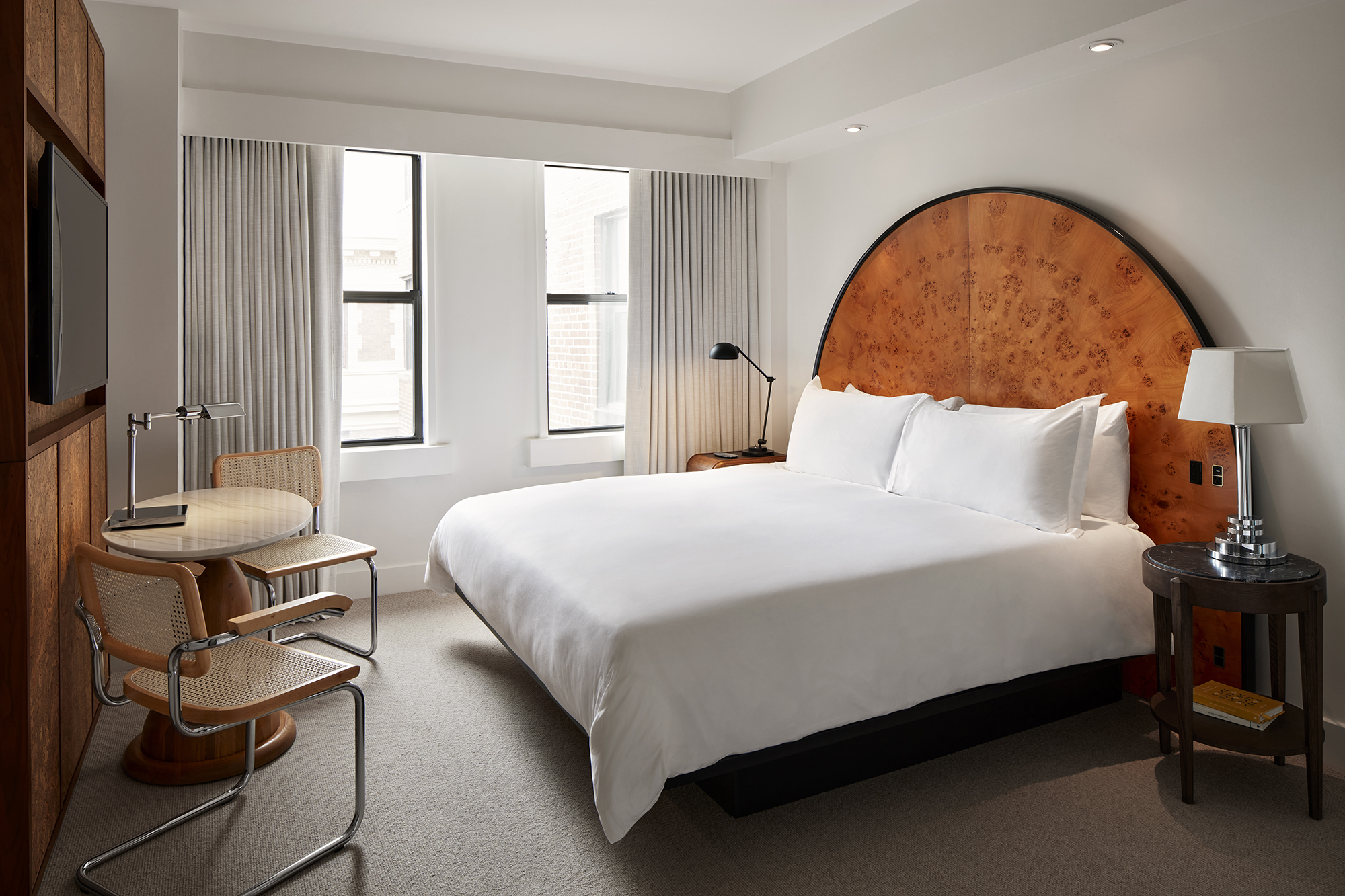 A modern hotel room at Lyle Washington DC, featuring a king-sized bed, arched wooden headboard, and minimalist decor.
